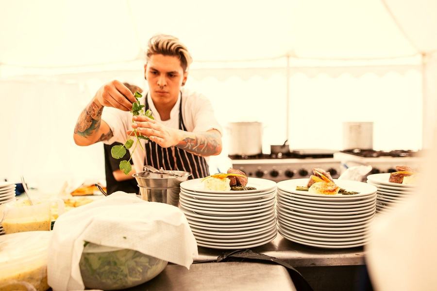 A chef plating food inside a catering marquee.