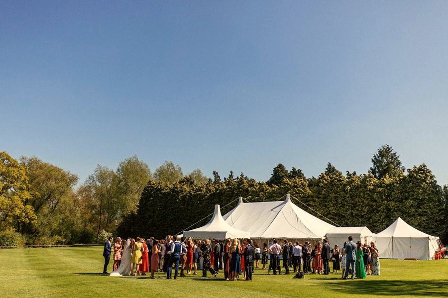 A wide shot of a wedding marquee on a lawn with guests gathering outside.