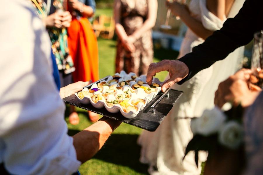 A waiter serving a tray of canapes to guests in a garden.